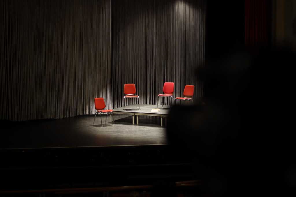 4 lehre Stühle auf der Bühne in einem Lichtkegel
