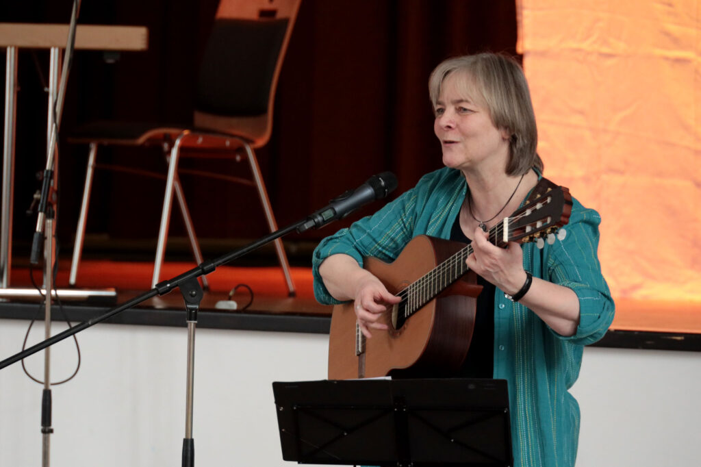 Eine Frau steht mit Gitarre am Mikrofon und singt mit einem Lächeln im Gesicht