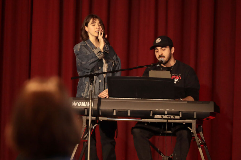 eine Sängerin steht neben einem Mann mit Bart, der an einem Keyboard sitzt.