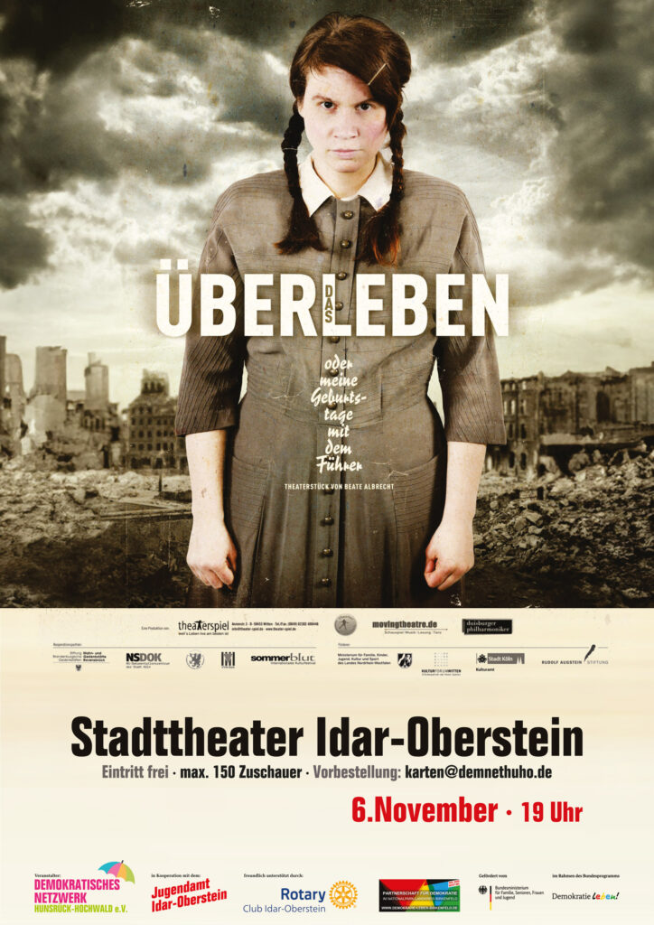 Plakat: eine junge Frau steht in einer zerbombten Stadt. Sie trägt ein tristes Kleid mit Kragen, das man in den 1940er Jahren trug. Ihre Haare sind zu zwei Zöpfen geflochten. Sie schaut ernst und entschlossen, ihre Hände sind fast zu Fäusten geschlossen und ihre Arme hängen seitlich herab.